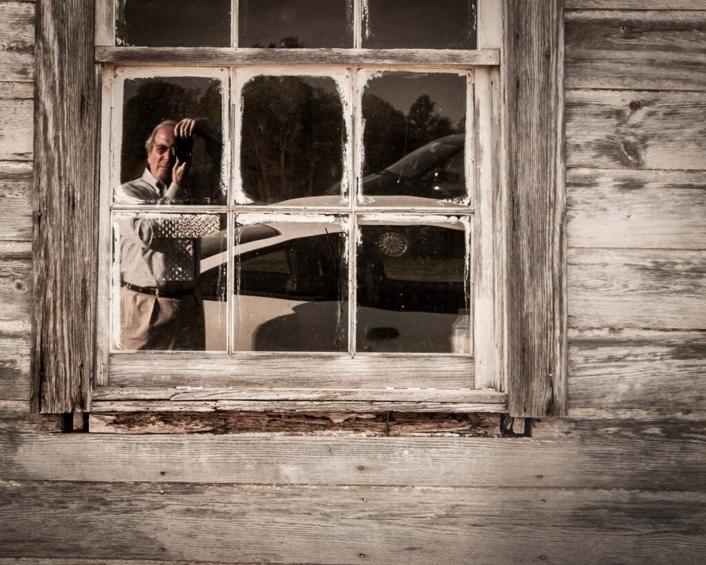 Bryan Hatchett. copyright, photograph of Bryan Hatchett, photographer and author and photographer of a book, Tidewater Spirit, photographing a distressed window in Providence Forge, Virginia